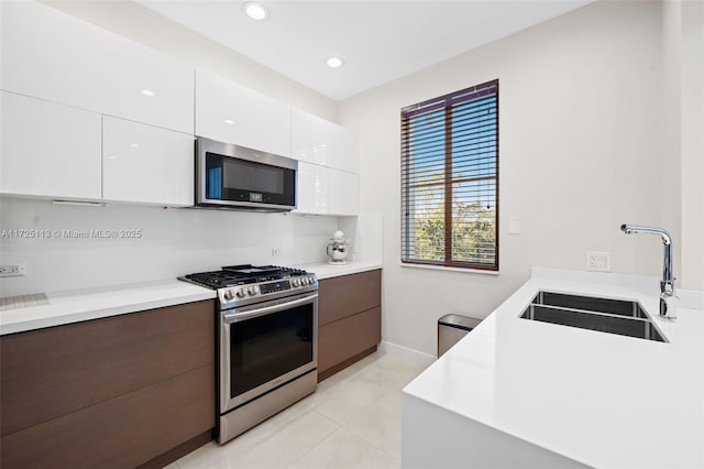 kitchen featuring white cabinetry, appliances with stainless steel finishes, light tile patterned flooring, dark brown cabinetry, and sink