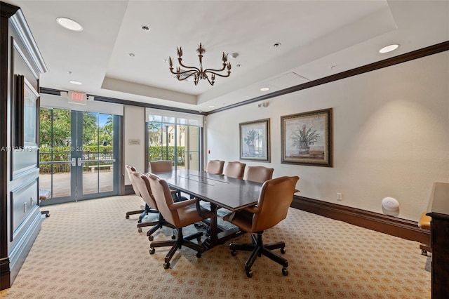 carpeted dining space with french doors, an inviting chandelier, a tray ceiling, and ornamental molding