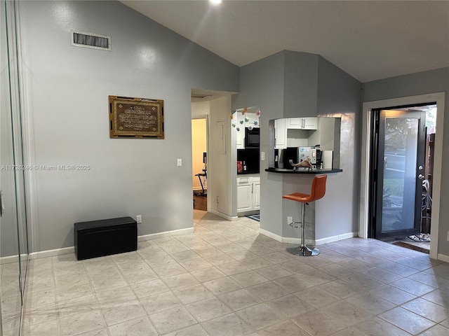 kitchen with lofted ceiling, light tile patterned floors, a kitchen bar, and white cabinetry