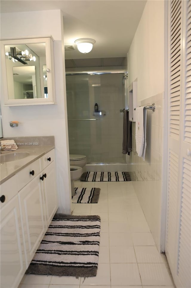 bathroom with toilet, vanity, tile patterned floors, a shower with shower door, and a bidet