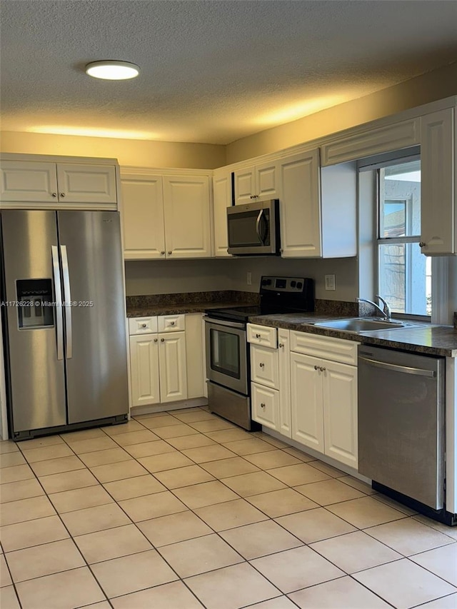 kitchen with sink, appliances with stainless steel finishes, light tile patterned floors, and white cabinetry