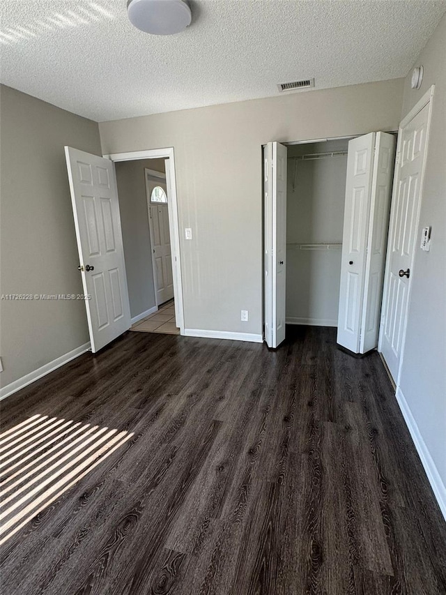 unfurnished bedroom with a textured ceiling, a closet, and dark hardwood / wood-style floors