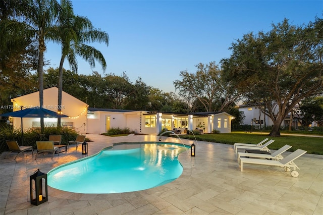 pool at dusk with pool water feature, a patio, and a yard