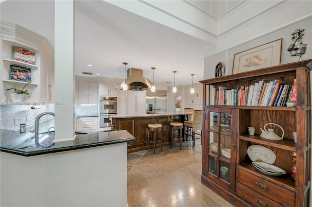 kitchen featuring kitchen peninsula, hanging light fixtures, island exhaust hood, decorative backsplash, and appliances with stainless steel finishes