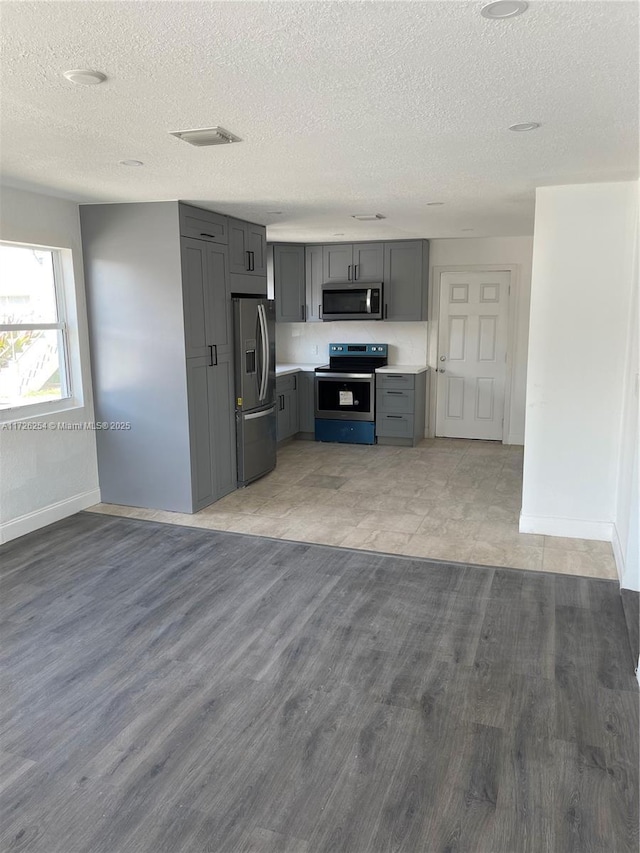 kitchen featuring a textured ceiling, appliances with stainless steel finishes, light hardwood / wood-style floors, and gray cabinets