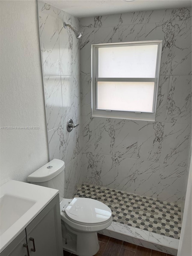 bathroom featuring a tile shower, vanity, and toilet