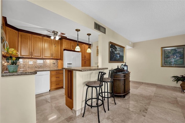 kitchen with white appliances, a kitchen breakfast bar, hanging light fixtures, ceiling fan, and backsplash