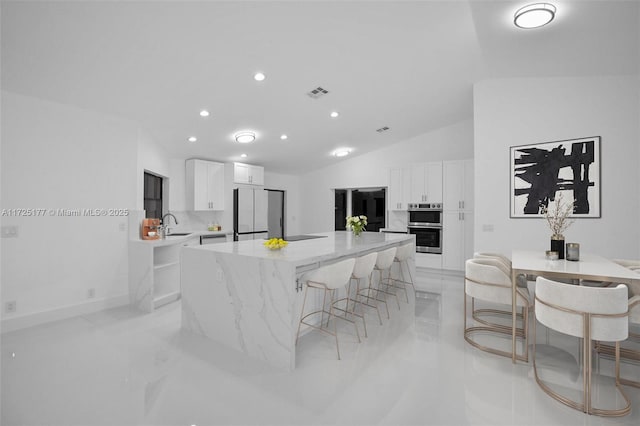 kitchen with white cabinets, refrigerator, a center island, and vaulted ceiling