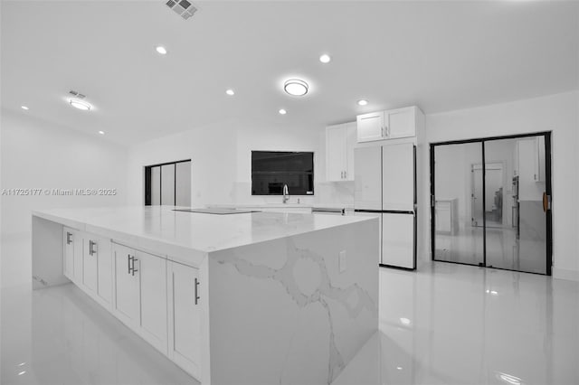 kitchen featuring light stone counters, a large island, white cabinetry, white refrigerator, and sink