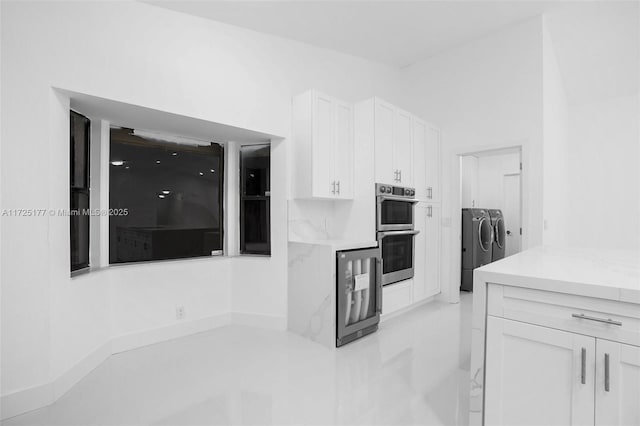 kitchen with washer and dryer, beverage cooler, stainless steel double oven, and white cabinetry