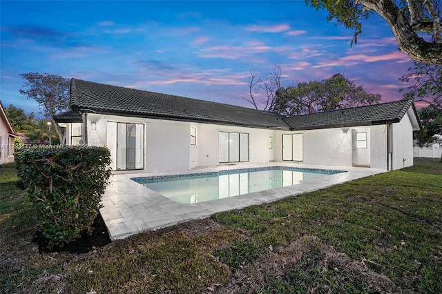 back house at dusk featuring a yard and a patio area