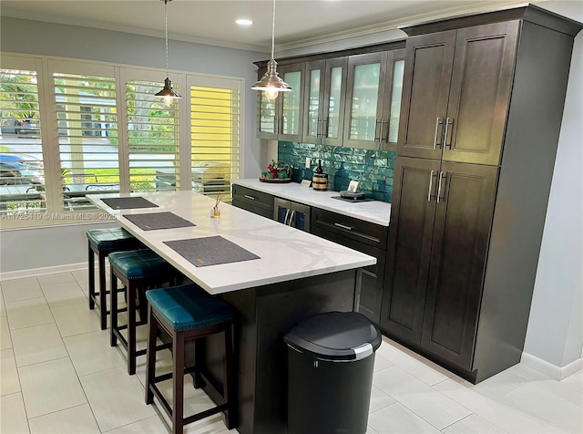 bar with decorative light fixtures, ornamental molding, tasteful backsplash, dark brown cabinetry, and light stone countertops