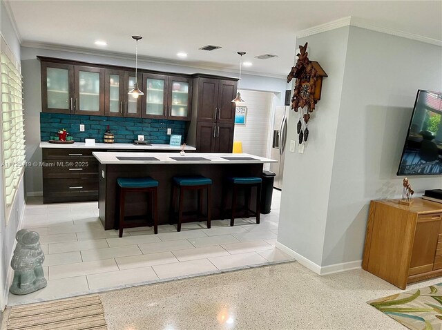 interior space featuring pendant lighting, a kitchen bar, a kitchen island, dark brown cabinetry, and backsplash