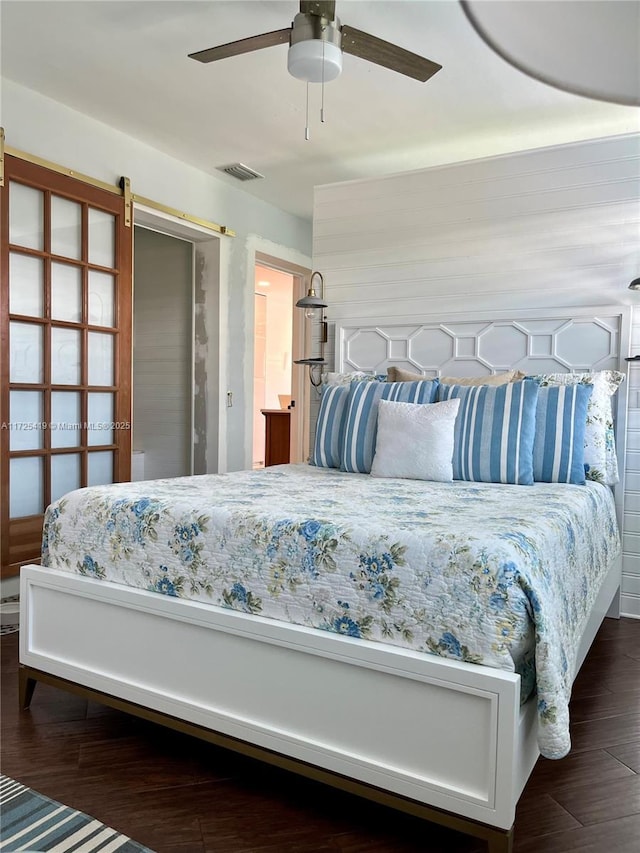 bedroom with ceiling fan, a barn door, and dark wood-type flooring