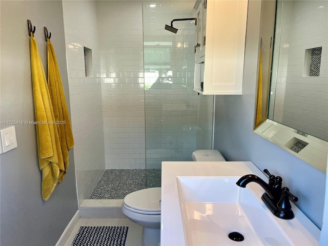 bathroom with toilet, vanity, tiled shower, and tile patterned floors