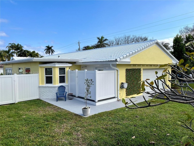 rear view of property featuring a lawn, a garage, and a patio