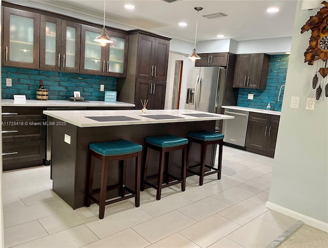 kitchen featuring pendant lighting, stainless steel appliances, a kitchen island with sink, backsplash, and dark brown cabinets