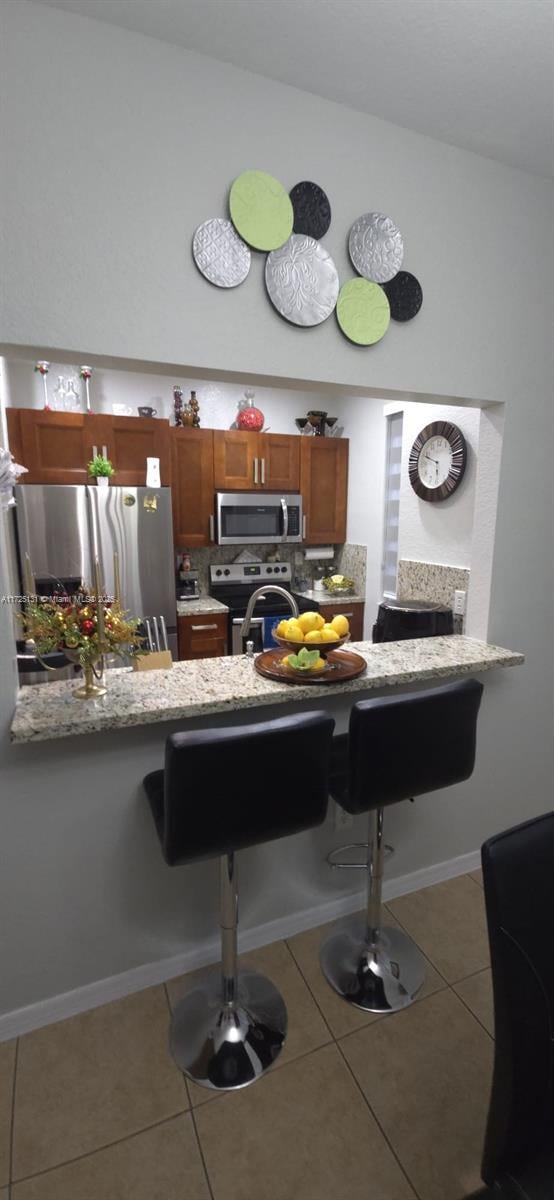 kitchen with tile patterned flooring, tasteful backsplash, kitchen peninsula, a breakfast bar area, and appliances with stainless steel finishes