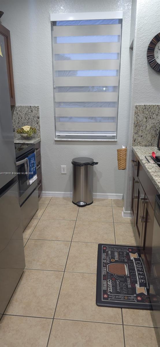 kitchen with stainless steel appliances, light stone counters, and light tile patterned floors