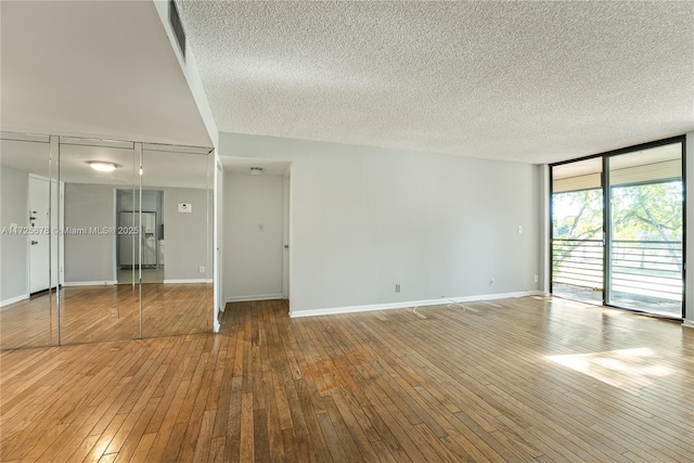 spare room with floor to ceiling windows, a textured ceiling, and hardwood / wood-style floors