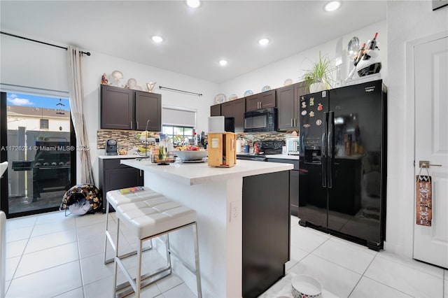 kitchen featuring light tile patterned flooring, a center island, black appliances, and light countertops