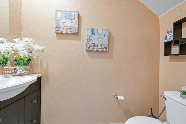 half bathroom with toilet, vanity, and a textured wall