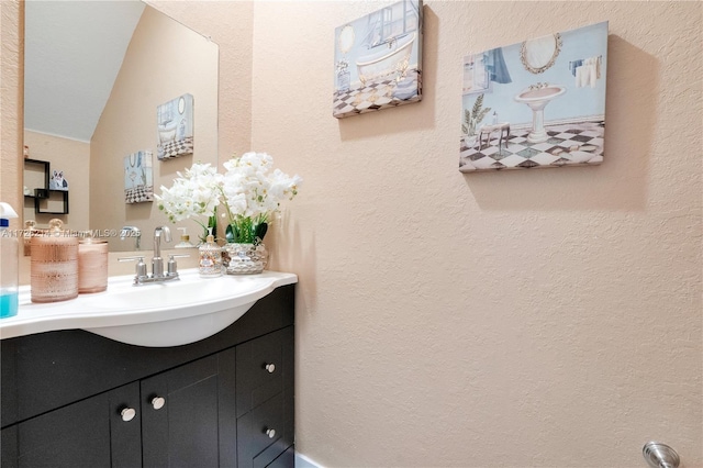 bathroom with vanity, lofted ceiling, and a textured wall