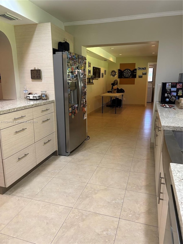 kitchen featuring light tile patterned flooring, ornamental molding, stainless steel fridge with ice dispenser, light stone countertops, and washer / dryer