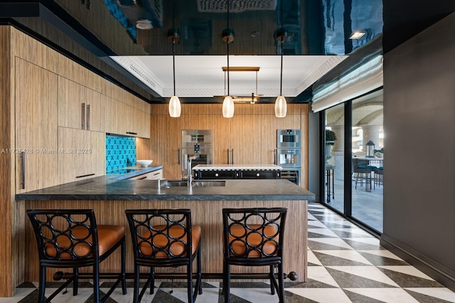 kitchen with kitchen peninsula, crown molding, hanging light fixtures, a breakfast bar area, and light brown cabinetry