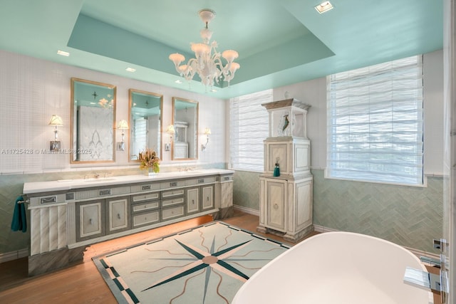 bathroom featuring double vanity, wood finished floors, a soaking tub, a sink, and a notable chandelier