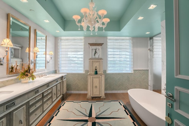 bathroom featuring double vanity, a freestanding tub, wood finished floors, a sink, and a notable chandelier