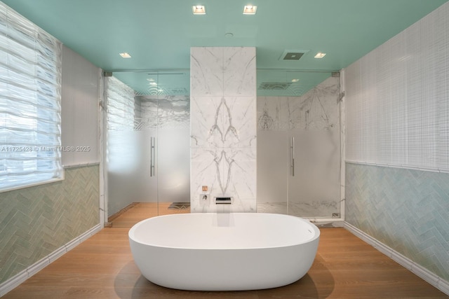 bathroom featuring tile walls, hardwood / wood-style floors, and plus walk in shower