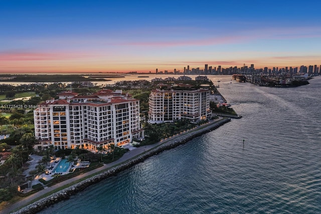 aerial view at dusk featuring a water view, a city view, and a view of the beach