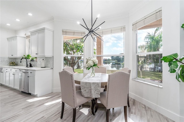 dining space featuring sink, light wood-type flooring, an inviting chandelier, and ornamental molding