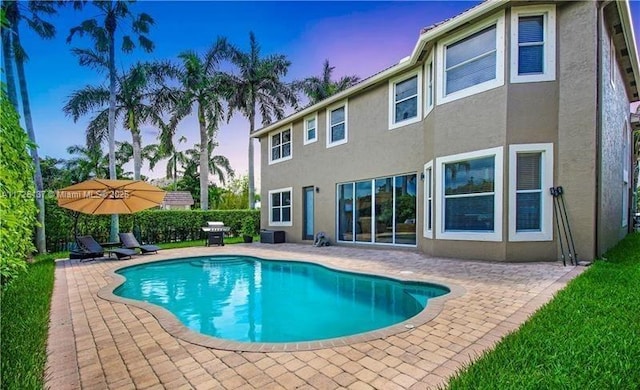 pool at dusk featuring a patio area and area for grilling