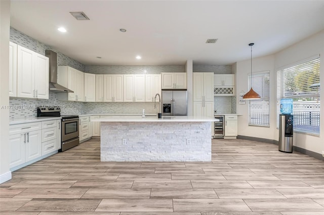 kitchen with white cabinetry, appliances with stainless steel finishes, beverage cooler, wall chimney range hood, and pendant lighting