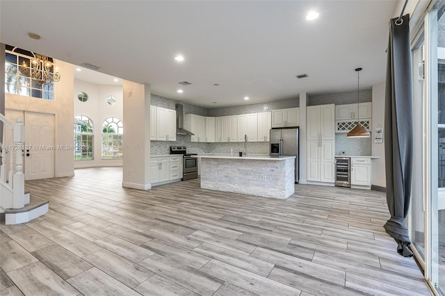 kitchen featuring appliances with stainless steel finishes, beverage cooler, hanging light fixtures, wall chimney range hood, and white cabinets