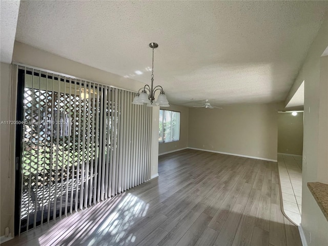 unfurnished dining area featuring ceiling fan with notable chandelier, a textured ceiling, and wood-type flooring