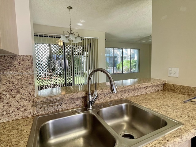 kitchen featuring sink, hanging light fixtures, a notable chandelier, and a textured ceiling