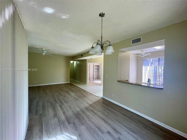 spare room with ceiling fan with notable chandelier, a textured ceiling, and hardwood / wood-style floors