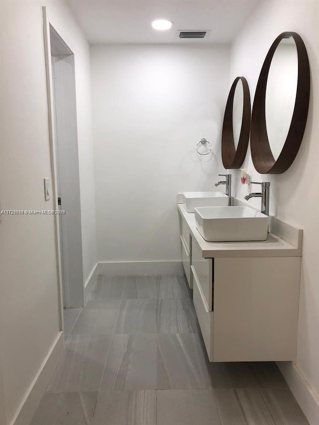 bathroom featuring double vanity, a sink, visible vents, and baseboards