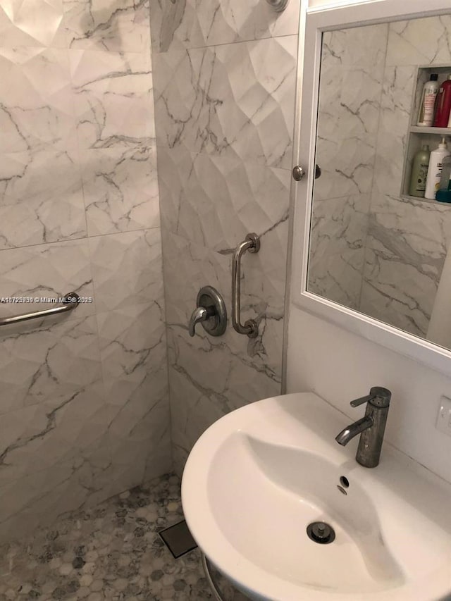 full bathroom with a marble finish shower and a sink