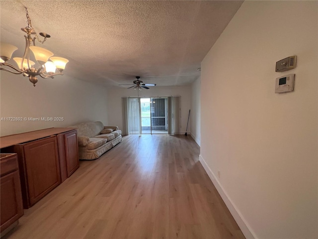 unfurnished living room with ceiling fan with notable chandelier, a textured ceiling, and light wood-type flooring