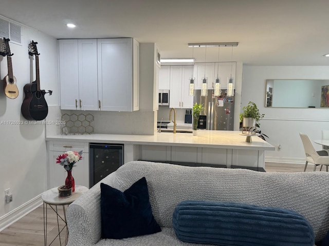 kitchen featuring stainless steel appliances, sink, white cabinets, kitchen peninsula, and wine cooler