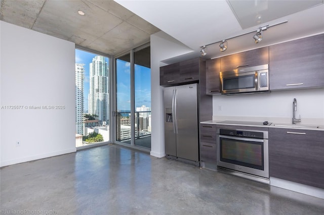 kitchen with concrete floors, a wall of windows, sink, dark brown cabinetry, and stainless steel appliances