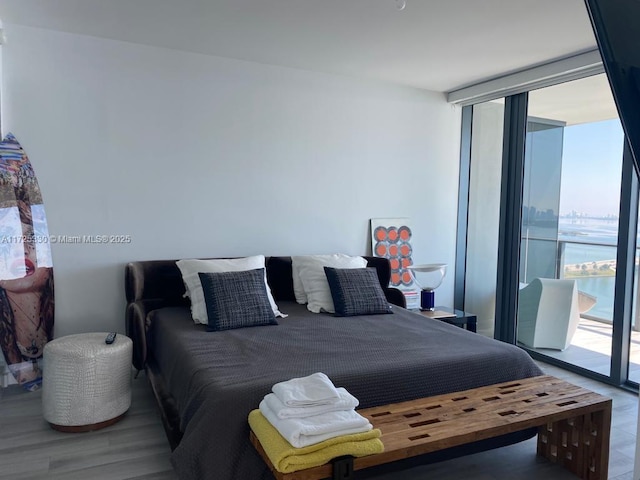 bedroom featuring access to outside, wood-type flooring, expansive windows, and a water view