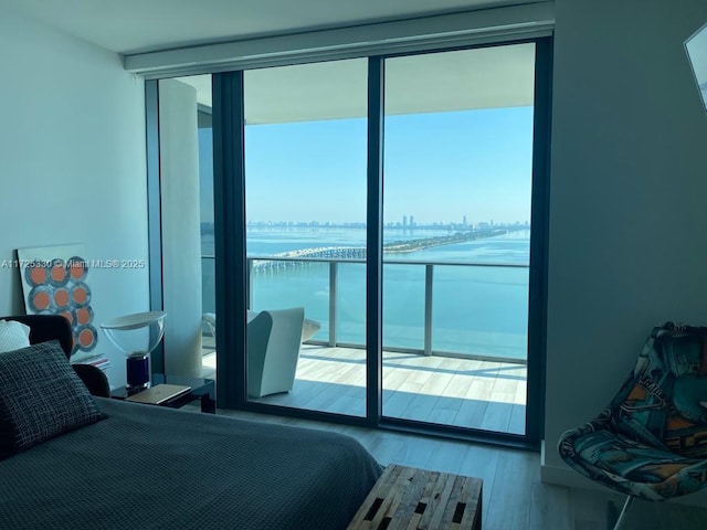 bedroom with light hardwood / wood-style floors, access to outside, a water view, and expansive windows