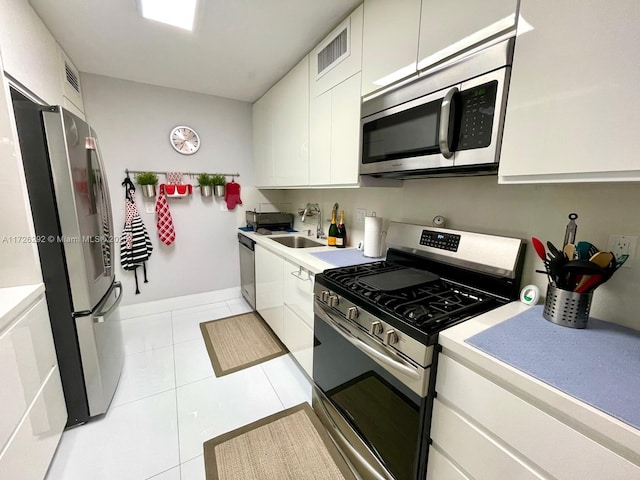 kitchen with appliances with stainless steel finishes, white cabinetry, sink, and light tile patterned floors