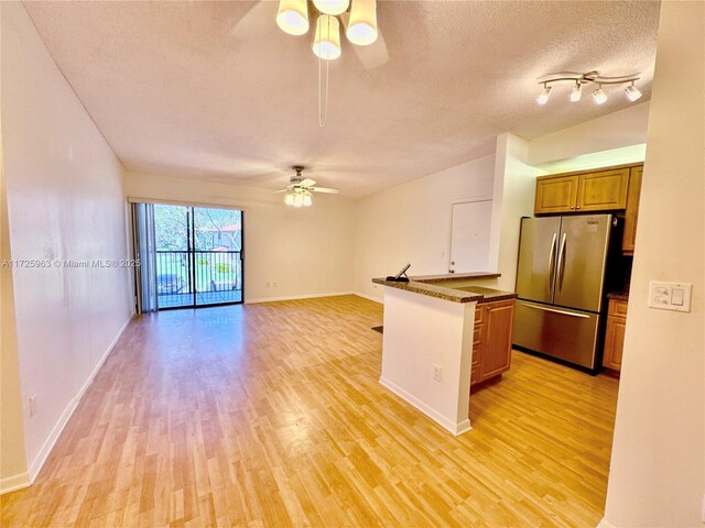 kitchen featuring light hardwood / wood-style flooring, stainless steel fridge, a breakfast bar, ceiling fan, and a textured ceiling