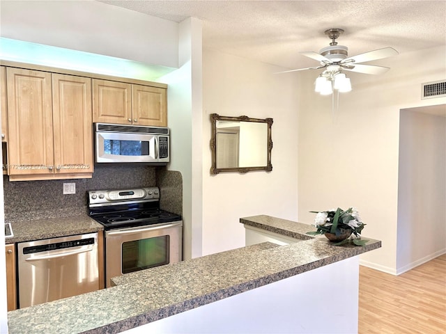 kitchen with appliances with stainless steel finishes, tasteful backsplash, ceiling fan, a textured ceiling, and light hardwood / wood-style flooring